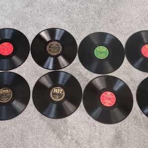 May include: A collection of ten black vinyl records with colorful labels, including red, green, and blue. The records are arranged in two rows on a gray surface, showcasing a variety of vintage music albums.