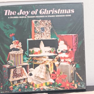 May include: A vintage vinyl record album titled "The Joy of Christmas." The album cover features a festive collage of Christmas-themed decorations, including wrapped gifts, a gingerbread house, and a Santa Claus figure, all set against a dark green backdrop.