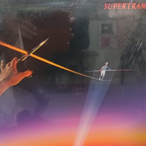 May include: A Supertramp vinyl record album cover featuring a tightrope walker with a hand reaching out towards a pair of glowing swords. The album cover has a gradient of colors from orange to purple.