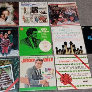 May include: A collection of vintage vinyl records featuring various artists and Christmas-themed albums. The album covers display diverse artwork, including portraits, illustrations, and festive decorations. The records are arranged on a gray surface.