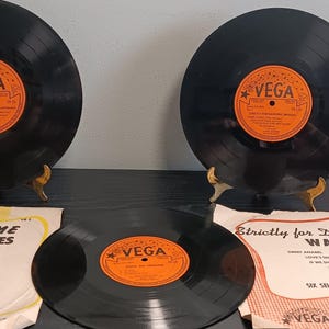 May include: Three black vinyl records with orange Vega labels, two displayed on gold stands. Two paper sleeves are included: one titled Dance Time Mixed Dances and the other Strictly for Dancing Waltzes, both featuring black text and decorative borders.