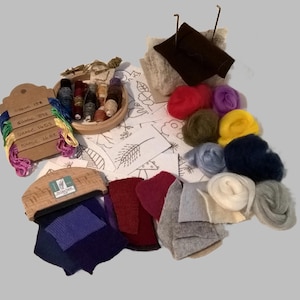 May include: A selection of craft materials, including embroidery floss, yarn, and fabric pieces. A wooden spool holds various coloured threads. A wooden tag displays the shade numbers. The colour palette includes shades of red, purple, blue, and green.