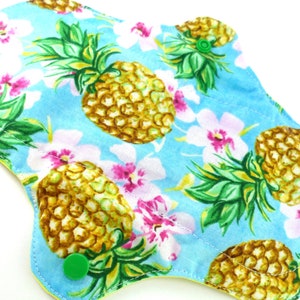 May include: A blue cloth pad with a pineapple and flower print. The pad has green snaps on the sides.