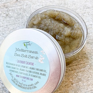 May include: A silver tin with a white label that reads "Jule Mediterranean Sea Salt Scrub - Lavender Jasmine - Mediterranean Sea Salt, Epsom Salt, Organic Sunflower Oil, Organic Coconut Oil, Organic Vegetable Glycerin, Organic Lavender Buds, Essential Oils, & Vitamin E Oil. www.tulebodycare.com 8 oz Mix Well before each use. Cover Lid Immediately After Using."