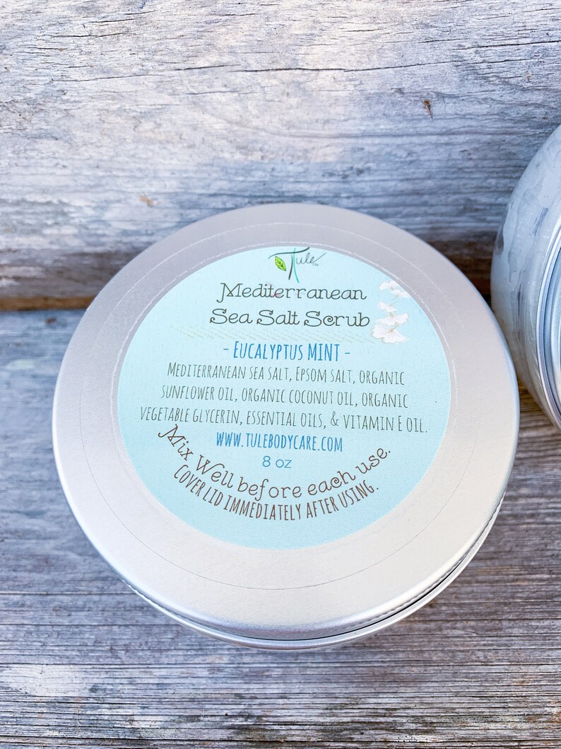 May include: A silver tin with a blue label that reads "Mediterranean Sea Salt Scrub - Eucalyptus Mint - Mediterranean Sea Salt, Epsom Salt, Organic Sunflower Oil, Organic Coconut Oil, Organic Vegetable Glycerin, Essential Oils, & Vitamin E Oil. www.tulebodycare.com 8 oz Mix Well before each use. Cover lid immediately after using."