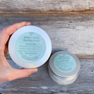 May include: Two silver tins of Mediterranean Sea Salt Scrub with Eucalyptus Mint scent. The label lists the ingredients: Mediterranean Sea Salt, Epsom Salt, Chegante Sunflower Oil, Organic Coconut Oil, Organic Vegetable Glycerin, Essential Oils, and Vitamin E Oil. The label also includes the website: www.tulebodycare.com. Each tin is 8 oz.
