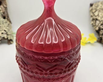 May include: A red glass jar with a decorative lid. The jar has a textured design and a scalloped lid.