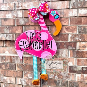 May include: Pink flamingo door hanger with white polka dots and the text "Let's Flamingle!"  The flamingo has a blue and white checkered bow and orange feet.