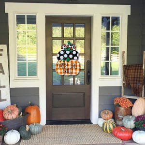 Peut inclure: Un porche d'entr&eacute;e d&eacute;cor&eacute; pour l'automne avec une pancarte en bois qui dit "FALL", une couronne avec le texte "Happy Fall Y'all" et des citrouilles de diff&eacute;rentes couleurs et tailles.