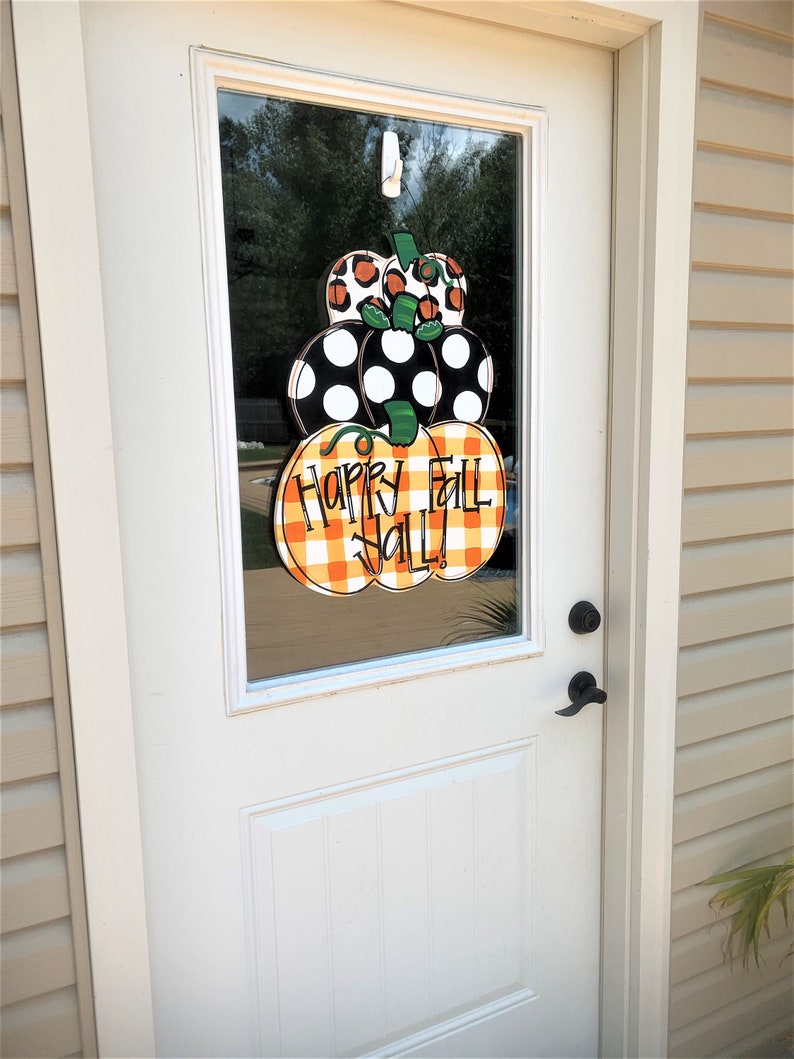 Peut inclure: Une porte blanche avec un panneau de verre repr&eacute;sentant une couronne de citrouille sur le th&egrave;me de l'automne avec le texte "Happy Fall Y'all!" en lettres vertes et noires.