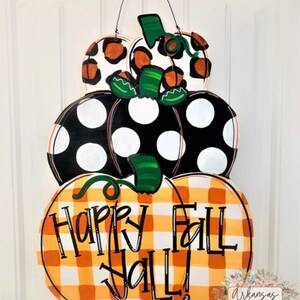 Peut inclure: Une pile de trois citrouilles en bois d&eacute;cor&eacute;es pour l'automne. La citrouille du bas est &agrave; carreaux orange et blanc avec les mots "Happy Fall Y'all!" La citrouille du milieu est noire avec des pois blancs. La citrouille du haut est blanche avec un imprim&eacute; l&eacute;opard noir et orange.