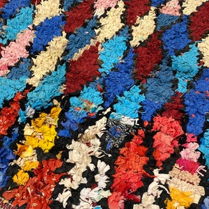 May include: A colourful Moroccan rug with a geometric pattern made from recycled fabric. The rug is made up of various colours, including red, blue, yellow, white, and pink.