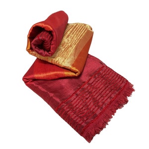 Puede incluir: Una bufanda de seda roja y dorada con borde de flecos. La bufanda está enrollada y atada con un nudo.