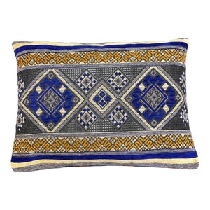 Puede incluir: Una almohada rectangular con un patrón geométrico azul, gris y dorado. La almohada tiene una textura tejida y una sensación suave y mullida.