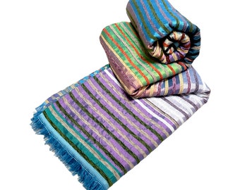 May include: Three colourful, striped silk throws. One is rolled up, displaying blue and green stripes. Another is folded, showing green and orange stripes. The third is spread out, with purple and blue stripes and a fringed edge.