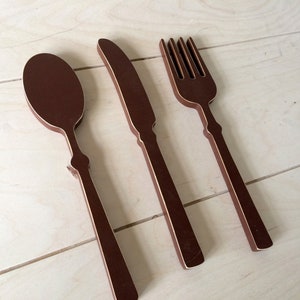 May include: A set of three wooden kitchen utensils in a brown color. The utensils are a spoon, a knife, and a fork.