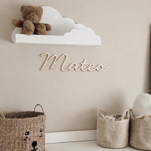 Peut inclure: Une chambre d'enfant avec une étagère blanche en forme de nuage avec un ours en peluche, et le nom "Mateo" en cursive. Des paniers en osier et une commode blanche avec des boutons en forme de nuage.