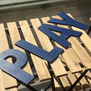 May include: Blue wooden letters spelling "PLAY" on a wooden table with a slatted top.