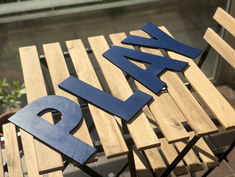 May include: Blue wooden letters spelling "PLAY" on a wooden table with a slatted top.