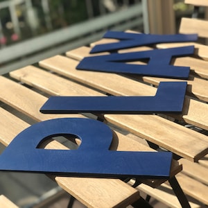 May include: Blue wooden letters spelling out the word "PLAY" on a light brown wooden surface.
