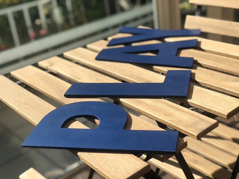 May include: Blue wooden letters spelling out the word "PLAY" on a light brown wooden surface.
