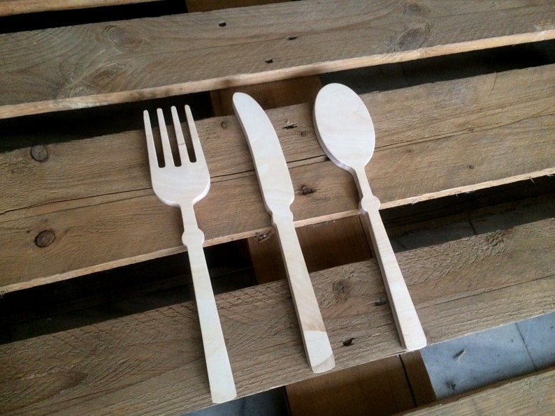 May include: A set of three wooden utensils, a fork, knife, and spoon, on a wooden surface.