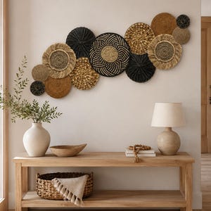May include: A collection of circular woven wall baskets in black, tan, and brown tones arranged in a cluster. The set includes various sizes and textures, featuring intricate patterns, coiled designs, and fringed edges for wall display.