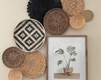 May include: A wall decor set featuring woven baskets and a framed print of a tropical plant. The baskets are in various sizes and shapes, with some featuring black and white geometric patterns. The framed print is in a light wood frame and features a green plant with large leaves.