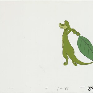May include: A green cartoon alligator holding a large green leaf in its right hand. The alligator is standing on a white background.