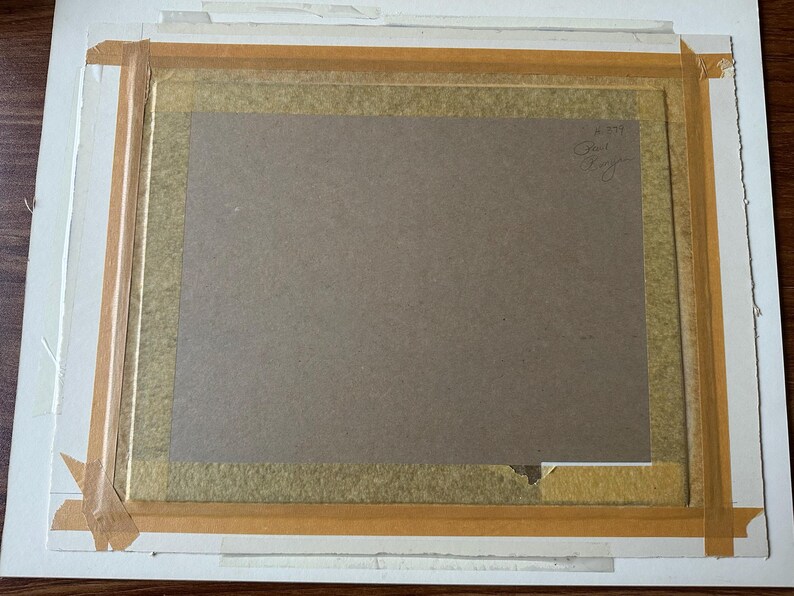 Puede incluir: La parte posterior de una obra de arte rectangular enmarcada con un soporte de cart&oacute;n marr&oacute;n asegurado con cinta adhesiva de color canela en los bordes. Una firma manuscrita y una peque&ntilde;a marca num&eacute;rica son visibles en la esquina superior.