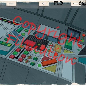 May include: A detailed illustration of a futuristic control panel with various buttons, switches, and a screen. The panel is made of gray metal with blue, green, red, and yellow accents.