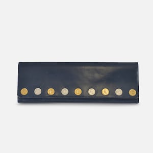 Puede incluir: Una cartera de cuero azul marino con una fila de botones met&aacute;licos decorativos. Los botones alternan entre tonos dorados y plateados. La cartera es rectangular y cerrada.