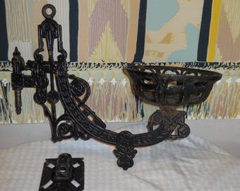 May include: Black cast iron wall-mounted sconce with ornate scrollwork and a decorative bowl. The sconce has a screw-on mounting bracket and a separate square base plate.