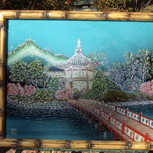 May include: A framed painting depicting a traditional Asian pagoda with a red roof and white walls. The pagoda is surrounded by trees and a lake with a bridge. The painting is set against a blue sky with white clouds.