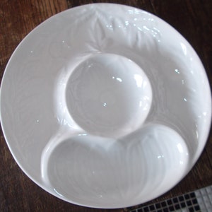 May include: White ceramic serving dish with three separate compartments. The dish has a decorative raised design around the edge.