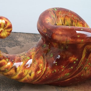 May include: A ceramic cornucopia with a brown, yellow, and green glaze. The cornucopia is shaped like a horn and has a wide opening at the top.