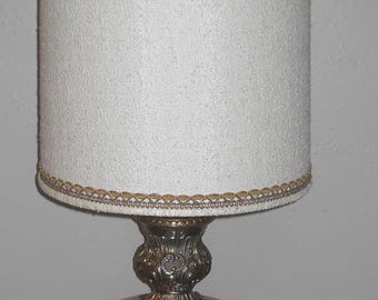 May include: A vintage table lamp with a white textured lampshade and a decorative gold trim. The base features a round, orange-red glass globe supported by ornate silver-toned metalwork. The lamp is a classic piece of home decor.