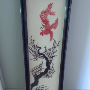 May include: A framed wall art piece featuring a red and pink phoenix bird with black and white branches and pink flowers. The artwork is made of shell pieces and is set against a white background.
