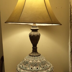 May include: A vintage table lamp with a white ceramic base featuring intricate blue and gold floral designs. The lamp has a yellow fabric shade.