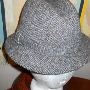 May include: A gray tweed fedora hat with a wide brim. The hat has a herringbone pattern and is made of a soft, textured fabric.
