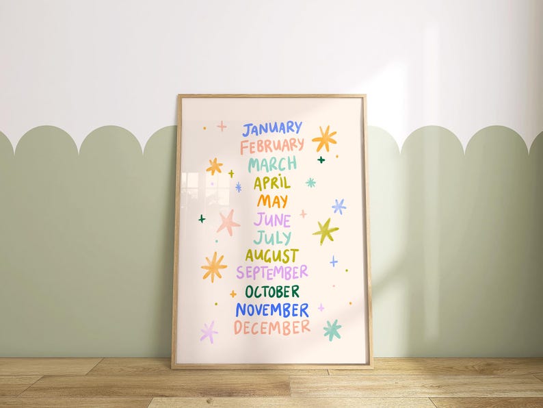 May include: A framed print featuring the months of the year in colorful text. Each month is written in a different color, with decorative starbursts. The background is a light beige color, and the frame is a light brown.