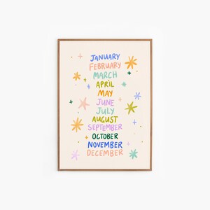 May include: A framed art print featuring the months of the year in a colorful, whimsical design. Each month is written in a different color, with decorative starbursts and plus signs. The print has a beige background and a brown frame.