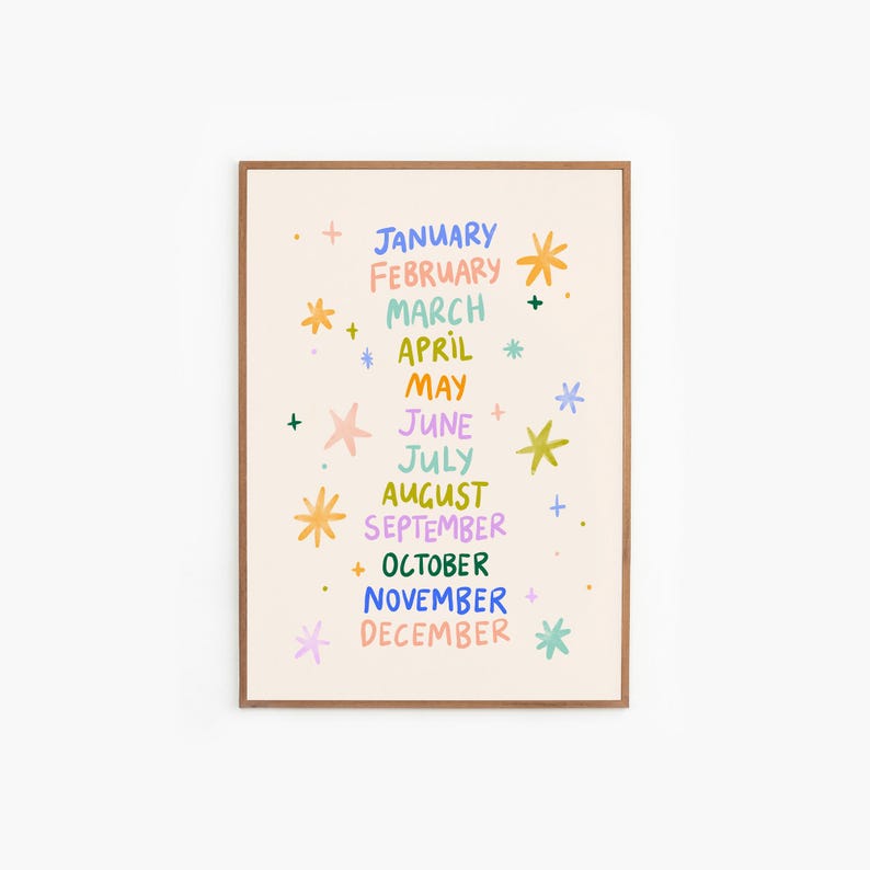 May include: A framed art print featuring the months of the year in a colorful, whimsical design. Each month is written in a different color, with decorative starbursts and plus signs. The print has a beige background and a brown frame.