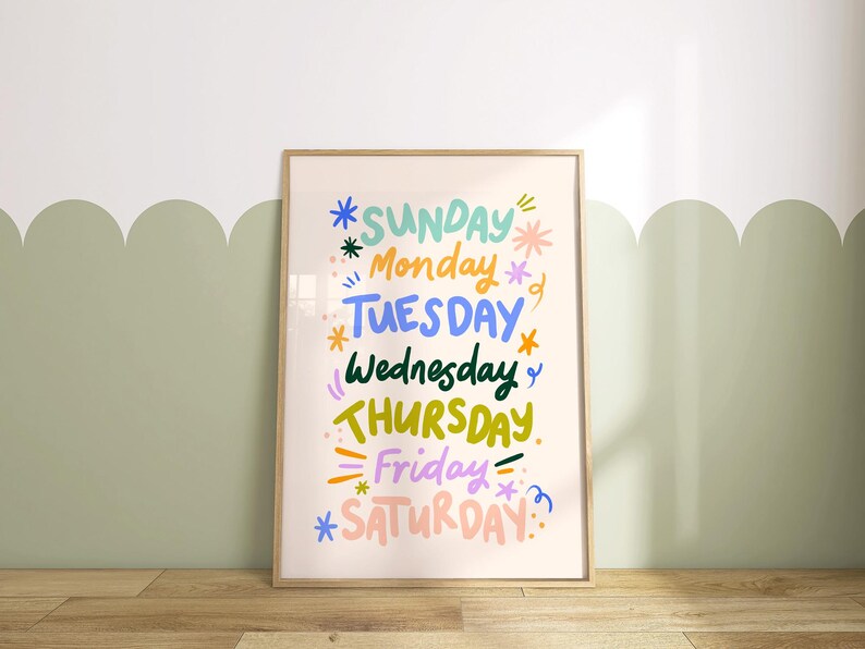 May include: A framed art print featuring the days of the week in colorful, whimsical lettering. The words are in various colors, including blue, green, yellow, and pink, with decorative star and line accents. The frame is a light wood color.