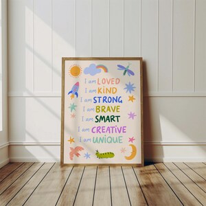 May include: A framed art print with the words "I am LOVED, KIND, STRONG, BRAVE, SMART, CREATIVE, UNIQUE" in colorful text. The print features illustrations of a sun, rocket, cloud, rainbow, dragonfly, stars, bird, caterpillar, and moon.