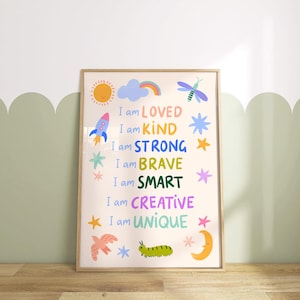 May include: A framed art print with the words "I am LOVED, KIND, STRONG, BRAVE, SMART, CREATIVE, UNIQUE" in colorful text. The print features illustrations of a sun, rocket, rainbow, stars, dragonfly, bird, caterpillar, and moon. The frame is light brown.