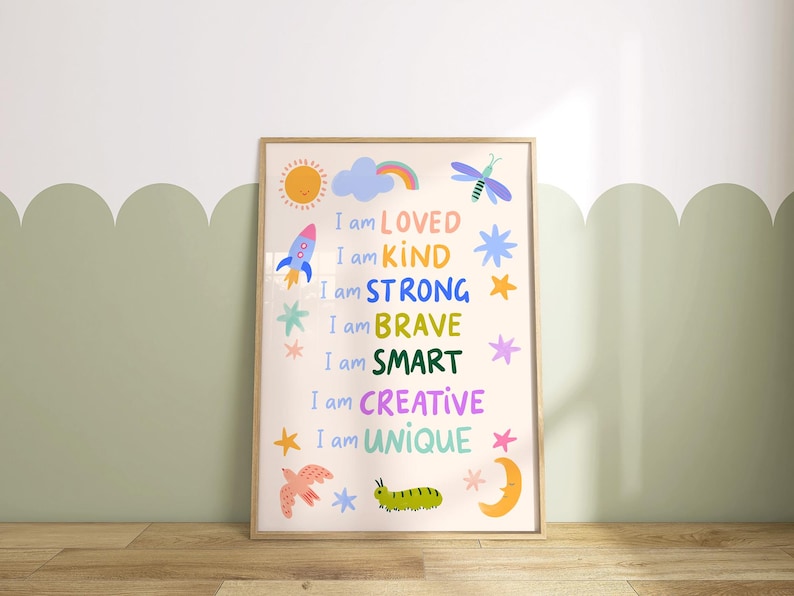 May include: A framed art print with the words "I am LOVED, KIND, STRONG, BRAVE, SMART, CREATIVE, UNIQUE" in colorful text. The print features illustrations of a sun, rocket, rainbow, stars, dragonfly, bird, caterpillar, and moon. The frame is light brown.