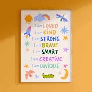 May include: A framed art print with the words "I am LOVED, KIND, STRONG, BRAVE, SMART, CREATIVE, UNIQUE" in colorful text. The print features illustrations of a sun, rocket, cloud with rainbow, dragonfly, stars, bird, caterpillar, and moon.