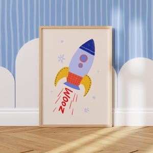 Könnte beinhalten: Ein gerahmter Druck mit einer Cartoon-Rakete im Flug. Die Rakete ist hellblau mit einer dunkelblauen Spitze, orangefarbenen und gelben Akzenten und dem Wort "ZOOM" in Rot. Der Hintergrund ist hellbeige.