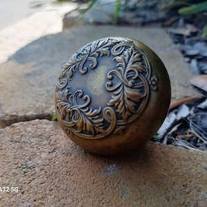 May include: A round, ornate, brass door knob with a floral design.